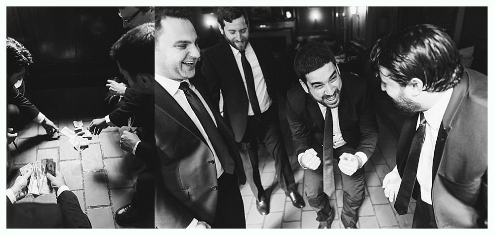 Five men in suits smile while someone performs a card trick in an indoor setting.