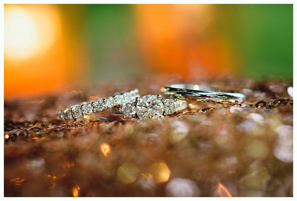 Three diamond wedding rings on a sparkly gold surface with blurred warm-toned background.