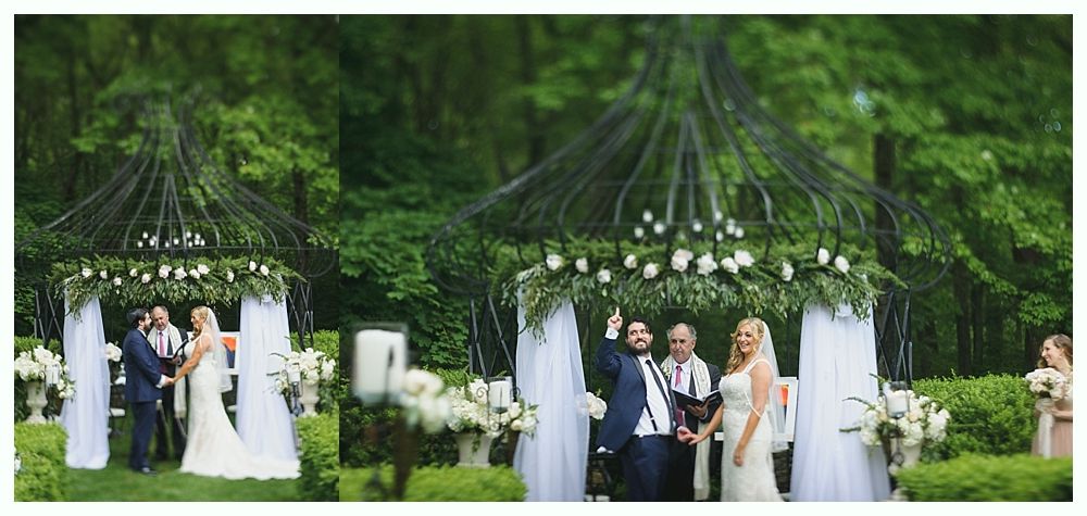 Wedding ceremony outdoors under a floral-decorated arch; couple with officiant; greenery background.