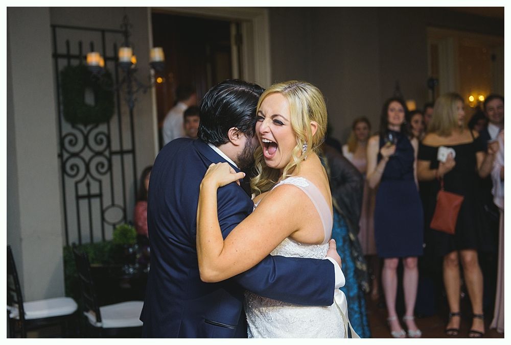 Bride and groom embrace, bride with joyous open mouth. Guests watch in an indoor setting.