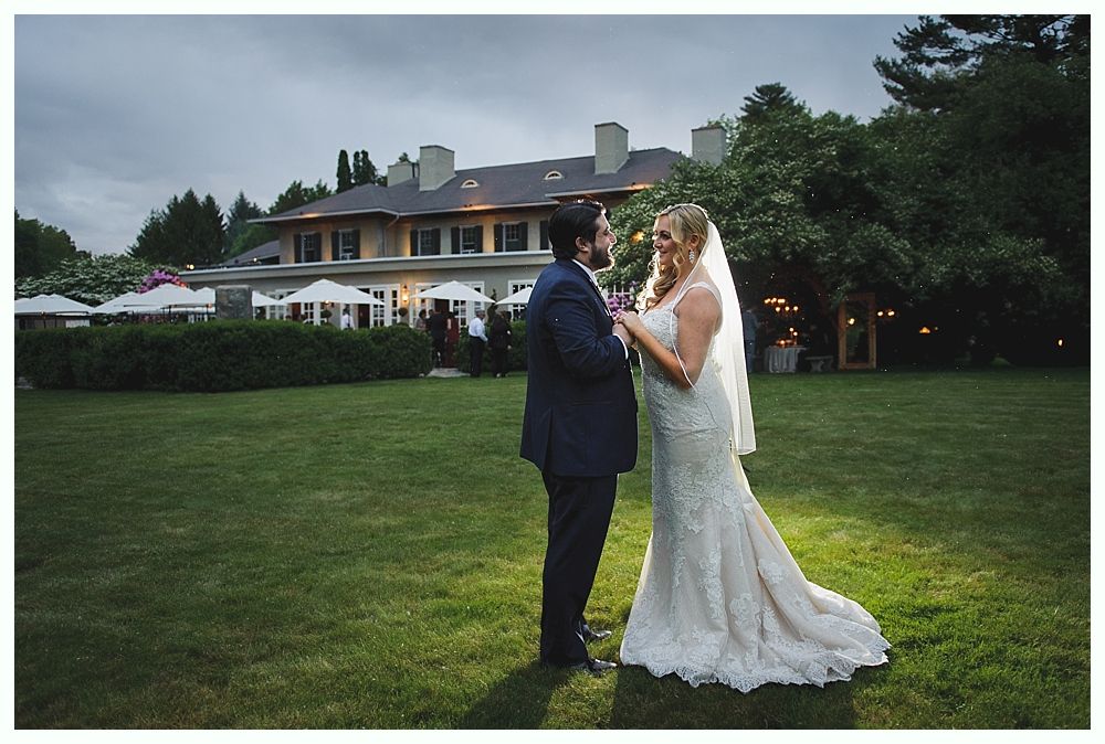Bride and groom facing each other on lawn, evening wedding at a mansion.