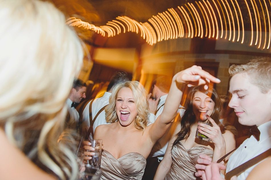 People dancing at a party under string lights; a woman with blonde hair cheers and raises her arm.