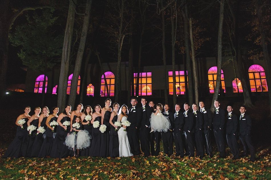 Wedding party in formal attire poses in front of a building with illuminated windows at night.