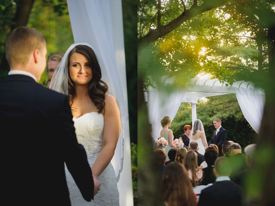 Bride and groom at outdoor wedding ceremony; bride smiles, holding groom's hand. White draped archway, guests.
