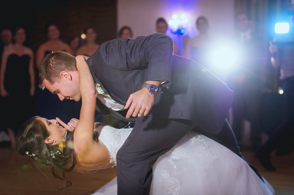 Bride and groom dancing, he dips her back as they smile at each other, bright light behind them.