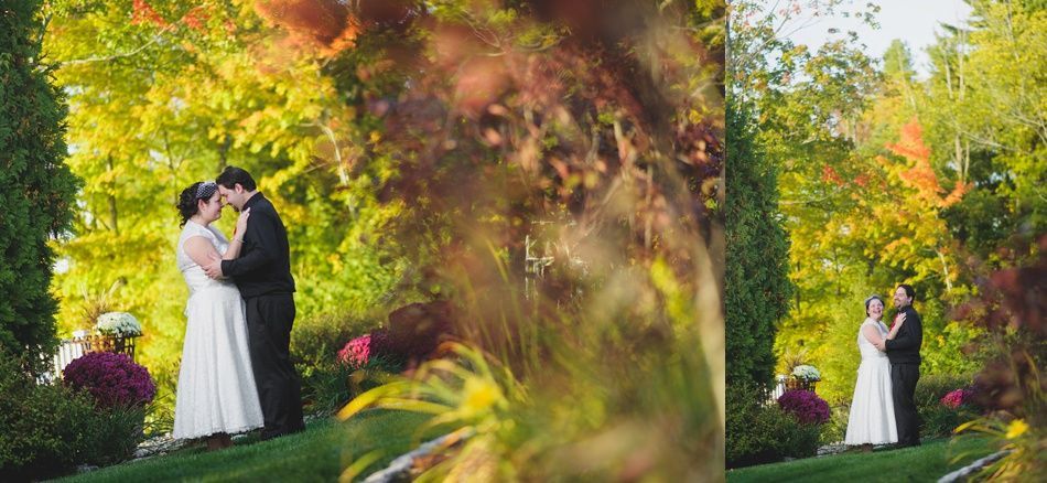 Couple in wedding attire embrace outdoors amidst autumn foliage and lush greenery.