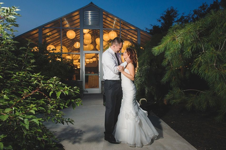Couple embraces outside a glass building lit with round lights; night.