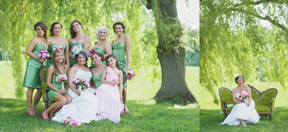 Wedding party poses outdoors by a tree. Bride and bridesmaids wear green dresses, seated on a green couch.