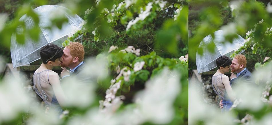 Couple kissing under an umbrella, surrounded by greenery and flowers.