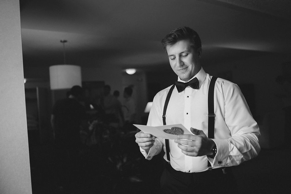 Man in a tuxedo reading a card, smiling, indoors.