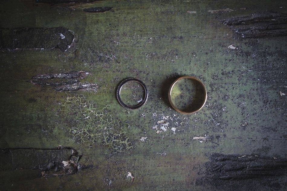 Two wedding rings, one silver, one gold, on a textured, weathered, green surface.