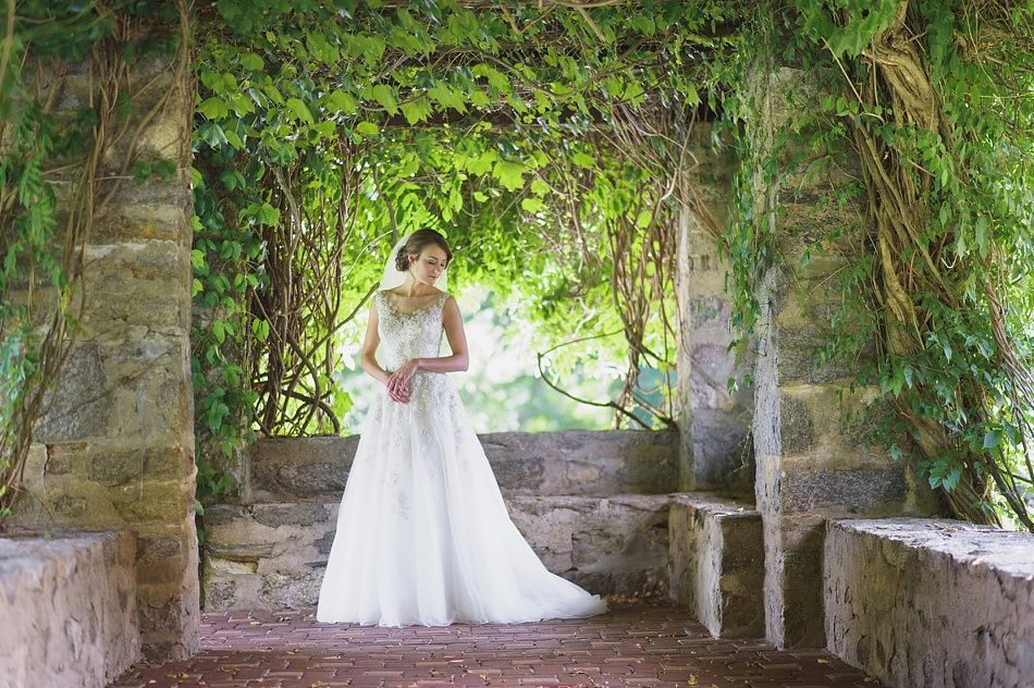 Woman in wedding dress stands in stone structure covered in vines.
