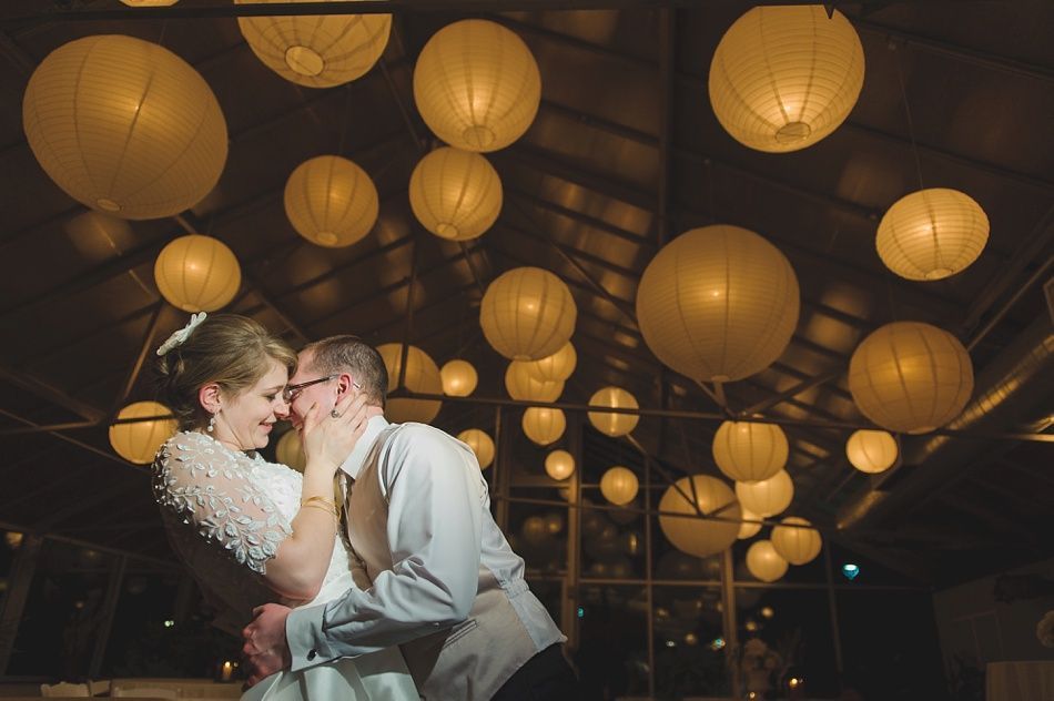 Couple dancing beneath glowing paper lanterns at a wedding reception.