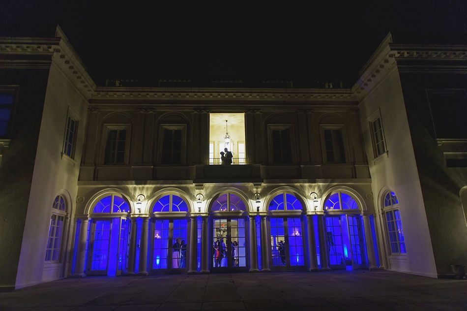 Lit up building exterior at night; blue lights frame arched windows and entrance, lit interior with figures.