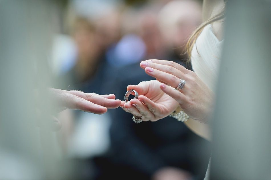 Ceremony hands exchanging rings, with audience in background.