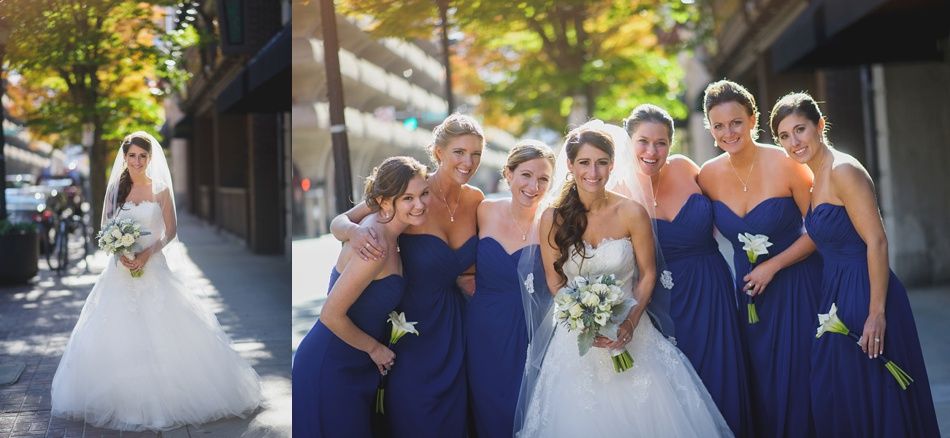 Bride and bridesmaids in navy blue dresses pose outdoors. Sunny day, holding bouquets, smiling.