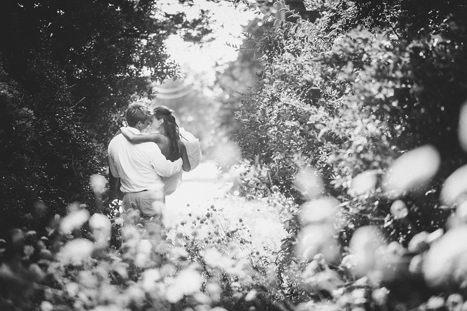 Couple kissing amid lush foliage, man holding woman. Black and white.