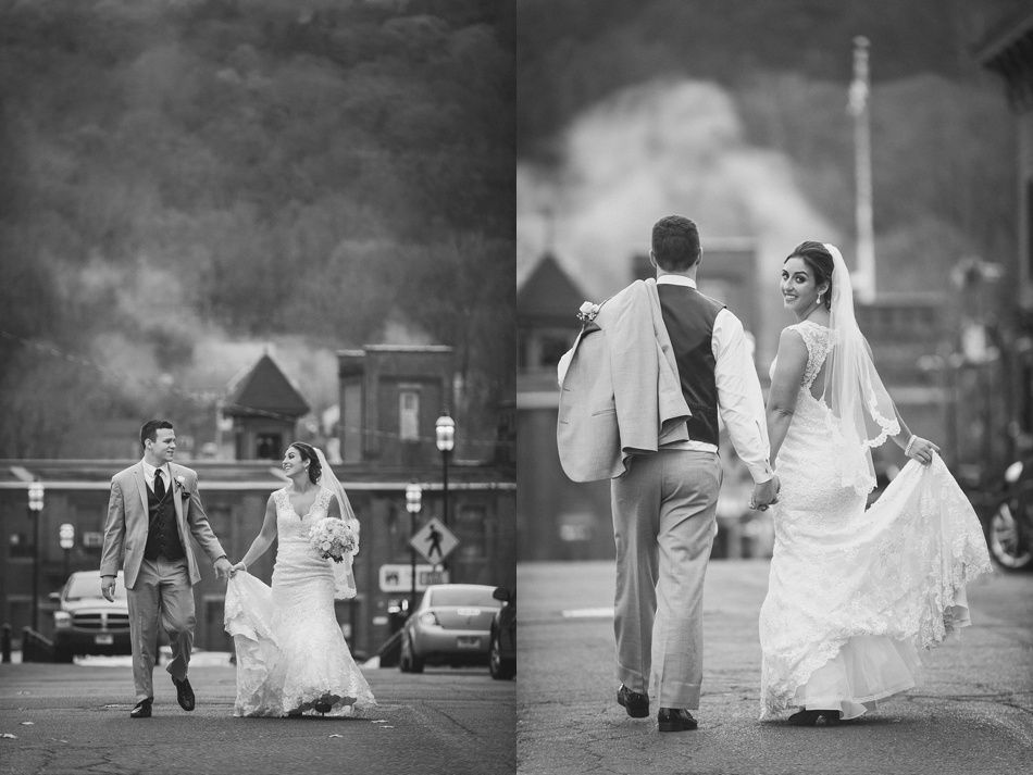 Bride and groom holding hands, walking down street, black and white, she smiles at camera.