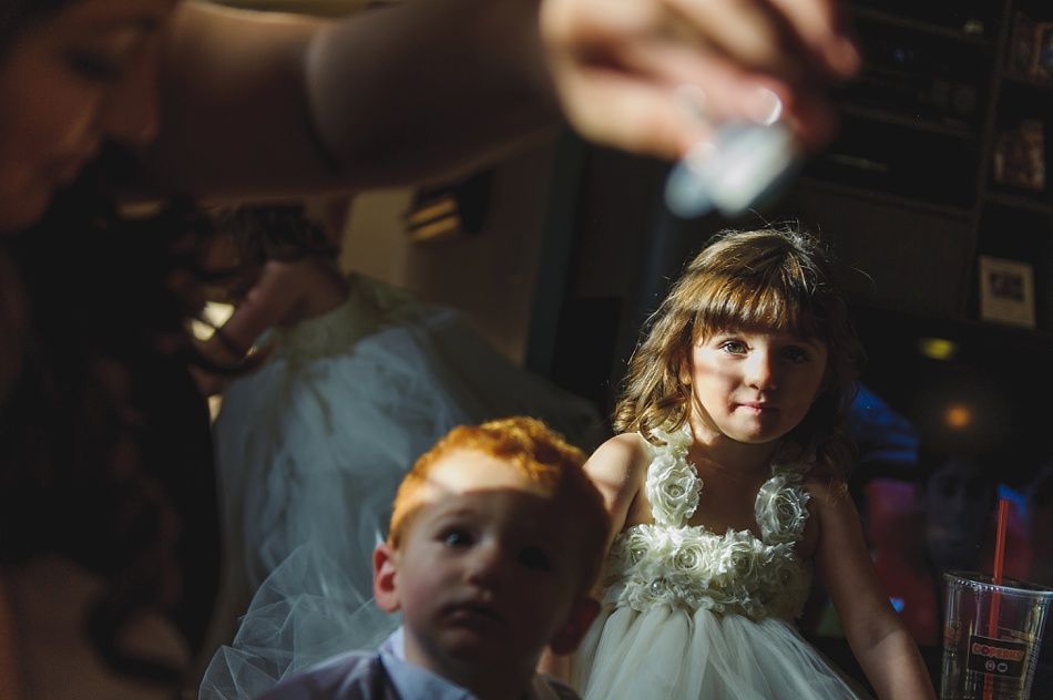 A young girl in a white dress and a boy with red hair sit indoors, lit by sunlight.