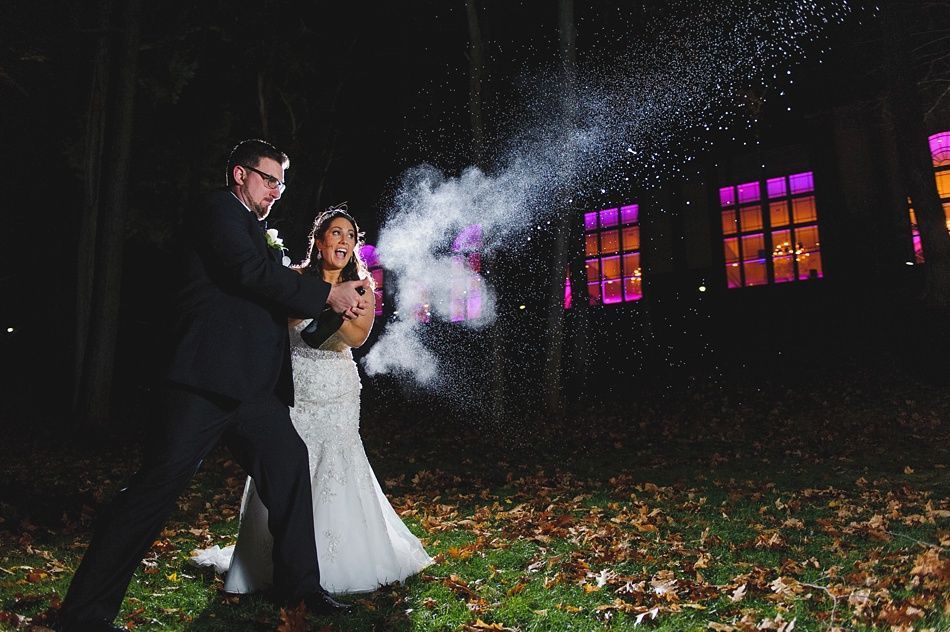 Couple popping champagne, spraying white mist. Night setting with lit windows.