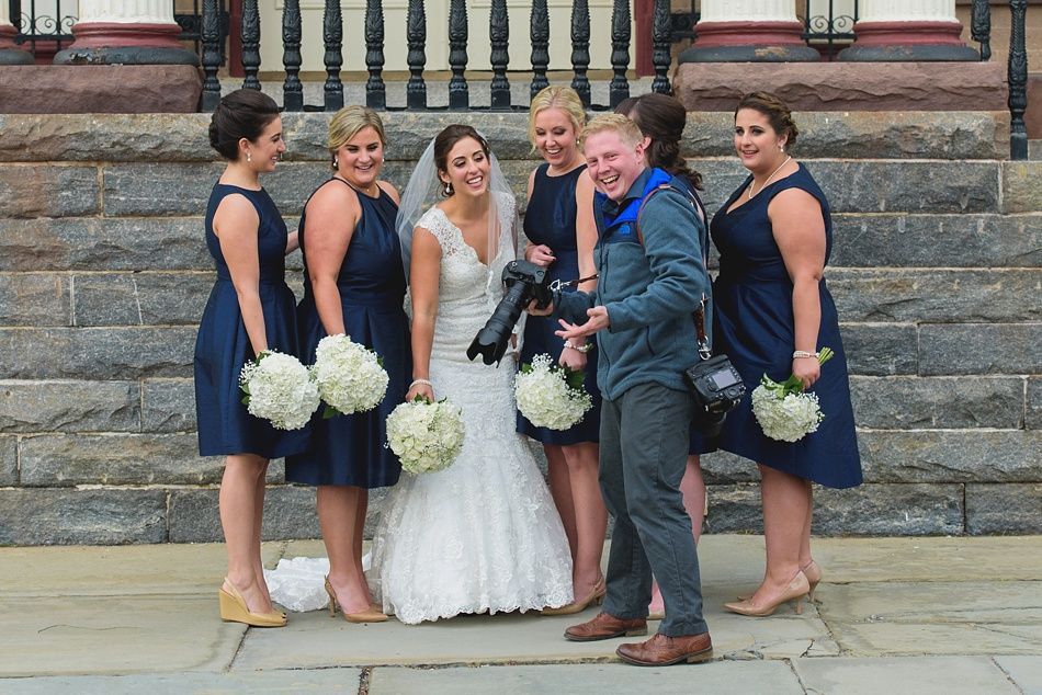Bride with bridesmaids and photographer on steps, bride laughing, all holding bouquets.
