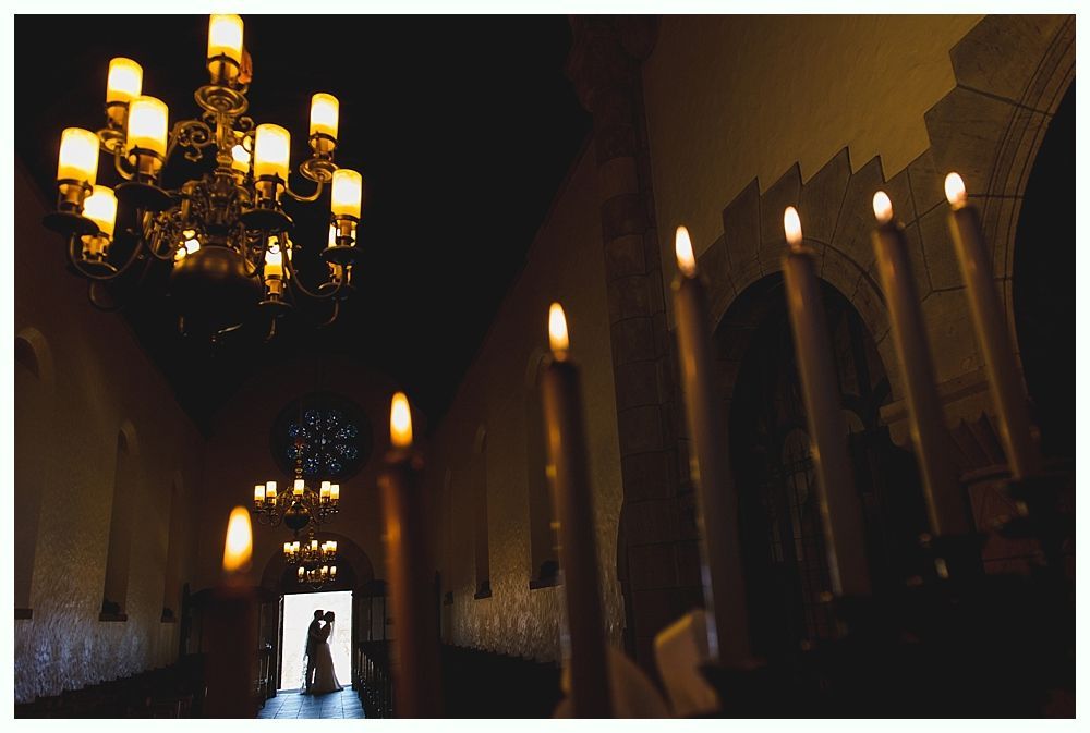 Interior church scene, lit by chandeliers and candles. Silhouetted figures stand in doorway.