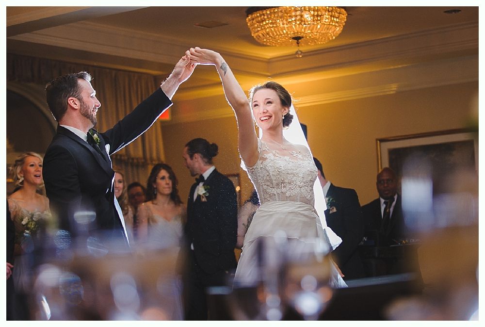 Bride and groom dancing at wedding reception, under chandelier.