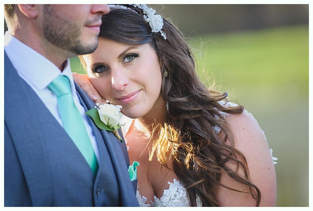 Bride and groom in formal attire, bride resting on groom's shoulder. Bride wears a white dress and headpiece, groom has a teal tie.