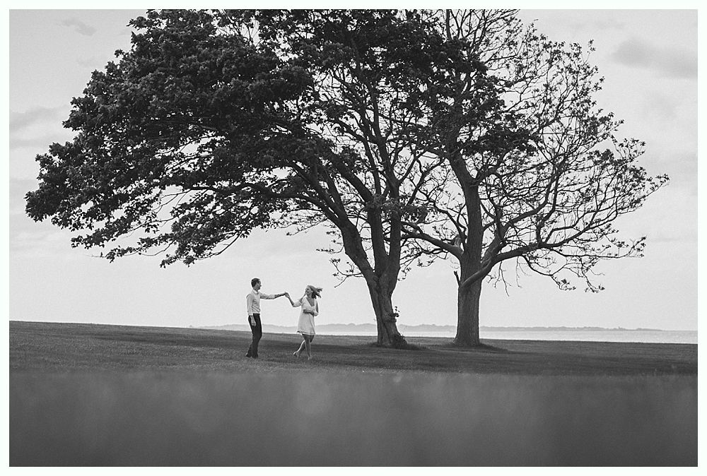 Couple holding hands under large tree on grassy hill.