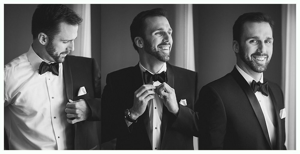 Man in tuxedo, adjusting bow tie, smiling, in front of a window. Black and white.