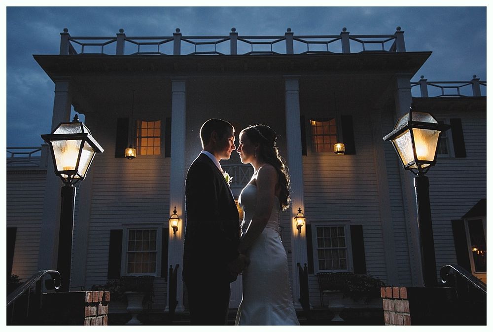 Couple embraces silhouetted in front of a white building with pillars and glowing lanterns.