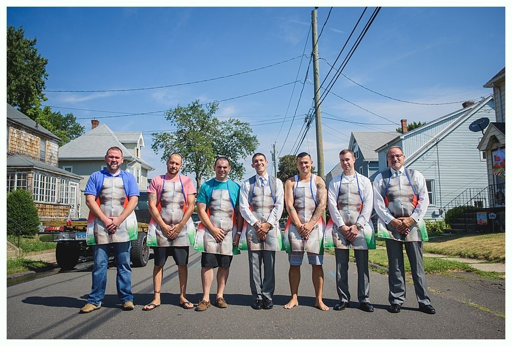 Group of men wearing aprons stand on a residential street; bright sunny day.