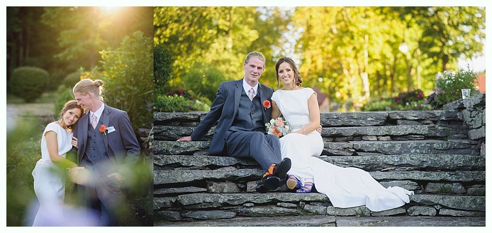 Wedding couple posing on stone steps; groom in suit, bride in white dress, smiling. Green trees in background.