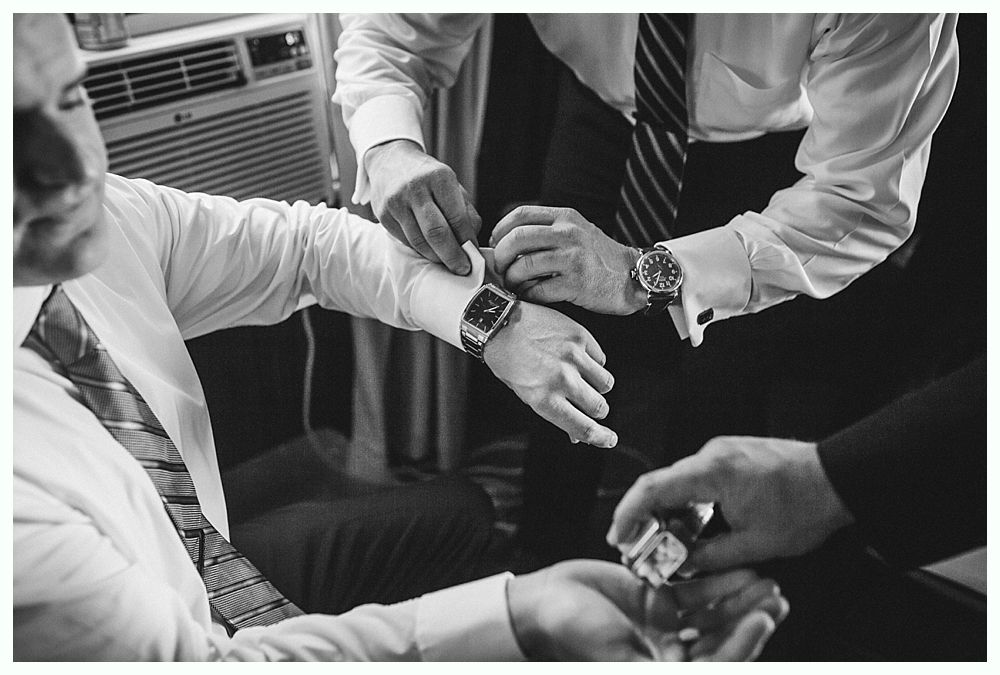 Three men in formal wear adjusting a watch on a wrist. Black and white.