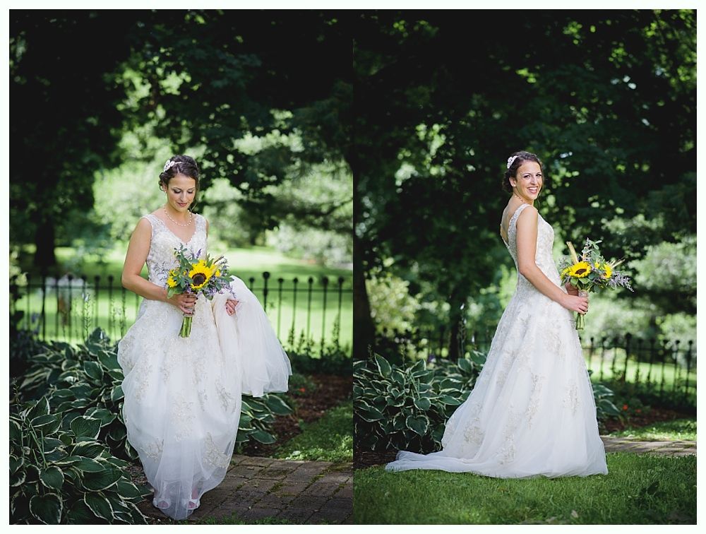 Bride in white gown holding sunflowers, standing outdoors near a fence and greenery.