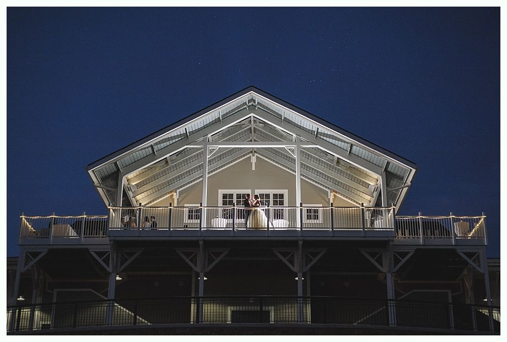 Couple on balcony of lighted building under a dark blue sky.