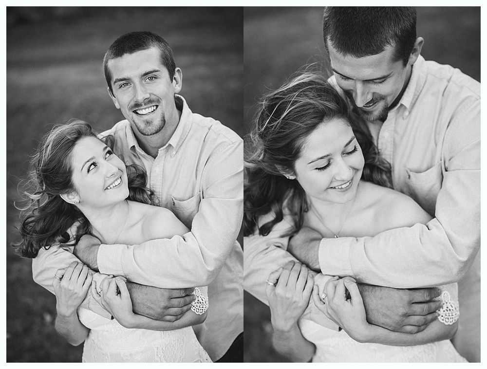 Couple embraces outdoors, smiling. Man hugs woman from behind. Black and white photo.