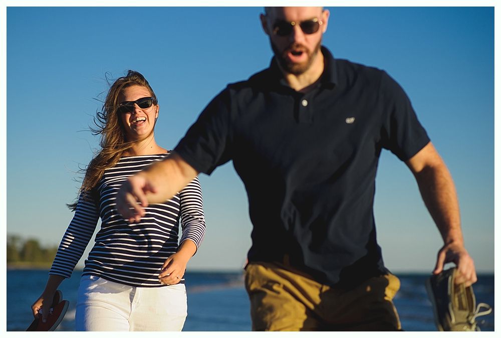 Woman in striped shirt and man in polo shirt outdoors; both wear sunglasses and appear happy.