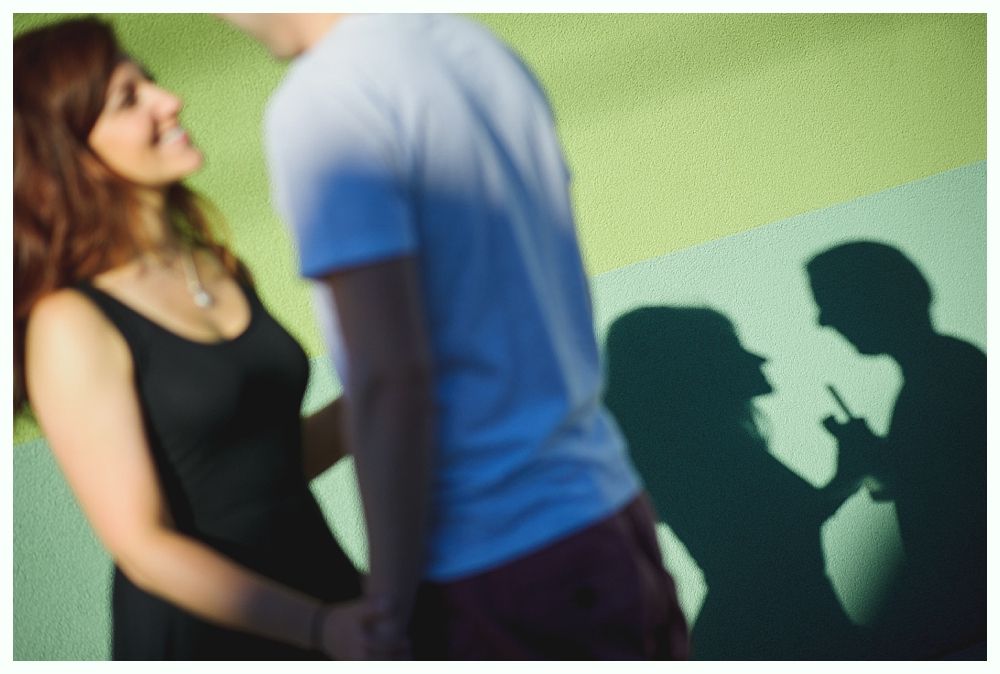 Couple holding hands, smiling. Shadows show them with a phone on a green wall.