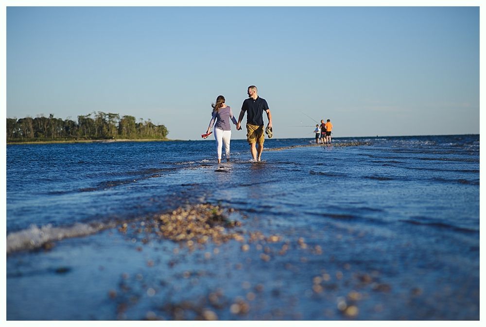 Couple holding hands, walking on a shallow water path towards the horizon, blue sky and water.