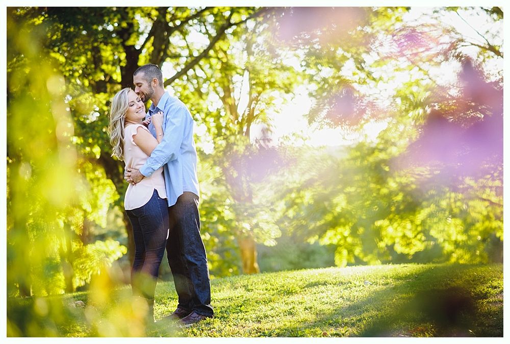 Couple embracing on a sunny green hillside, trees in background.