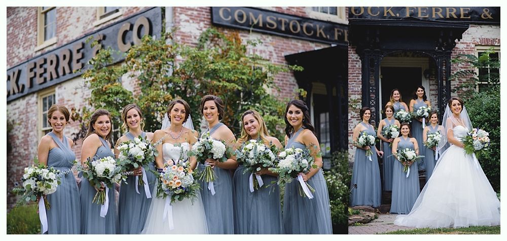 Wedding party poses outside a brick building. Bride in white dress, bridesmaids in gray dresses, holding bouquets.