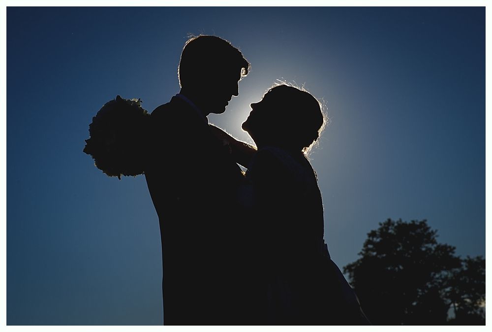 Silhouette of a couple dancing in front of the sun; the woman holds flowers.
