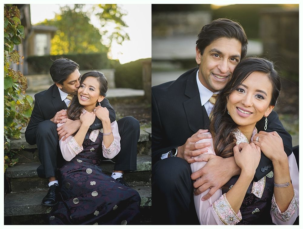 Couple embraces, smiling, outdoors. Man in suit kisses woman’s cheek, then hugs her. Sunlit steps and trees.
