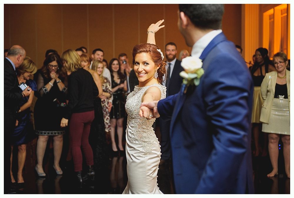 Bride dancing with groom at a wedding reception, guests watching.