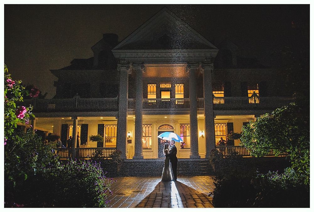 Couple with umbrella in front of a lit mansion at night during rain.