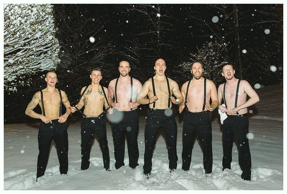 Six shirtless men in suspenders standing in snow, looking at the camera, with excited expressions.