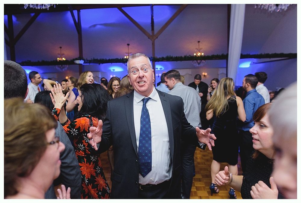 Man dancing at a party, arms wide, excited expression. People around him, festive atmosphere.