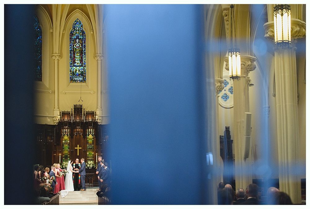 Wedding ceremony in a church; bride and groom at the altar; stained-glass window and chandeliers.