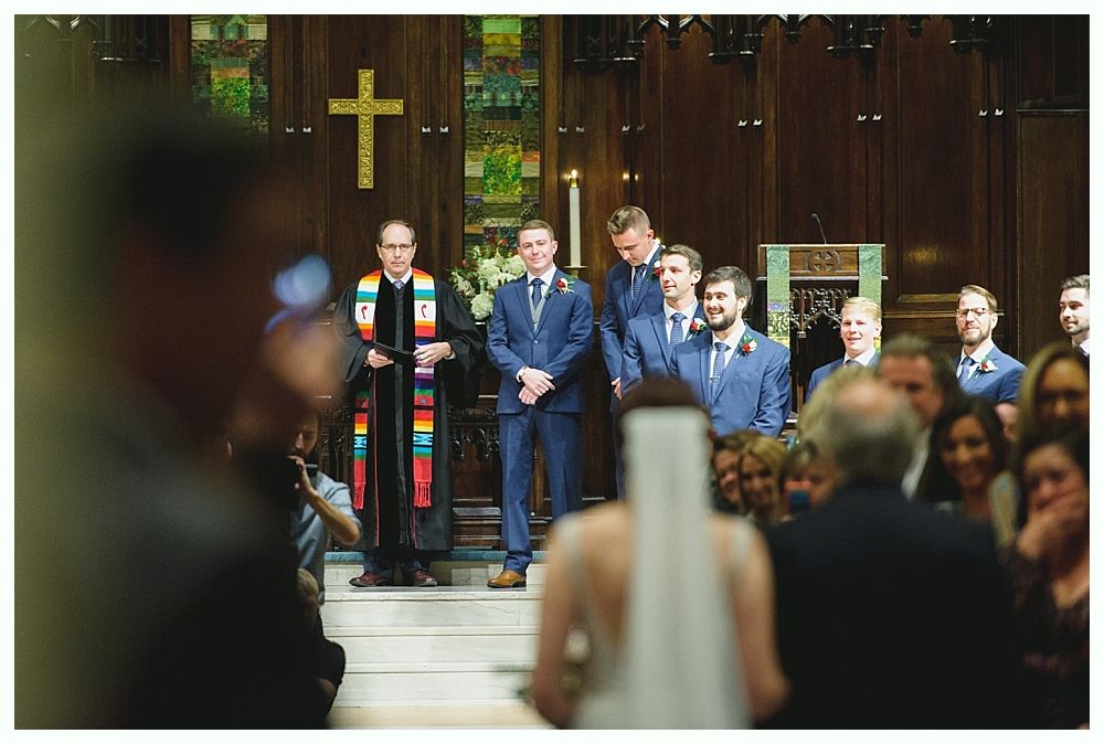 Wedding ceremony. Groom and groomsmen stand at the altar, awaiting the bride in a church. Priest in colorful stole.